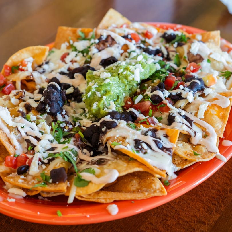 A vibrant plate of nachos with black beans, guacamole, cheese, and sour cream.